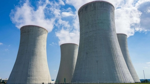 Four nuclear cooling towers of varying heights rising against a blue sky at a power generation facility