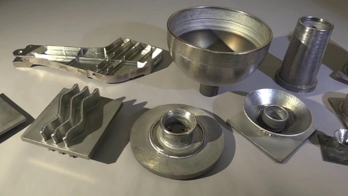 Several metal 3D-printed components including bowls, fins, and cylinders arranged on a flat grey surface